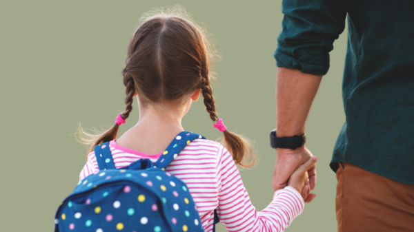 Back view of a young girl with braided hair and a polka dot backpack holding hands with her parent, symbolising support and guidance on her first day of school.