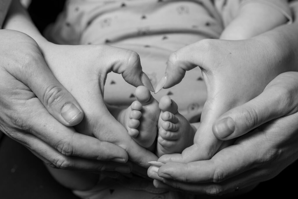 Parents forming heart shapes with their hands around the feet of a newborn baby, symbolizing love, unity, and shared responsibility in supporting breastfeeding.