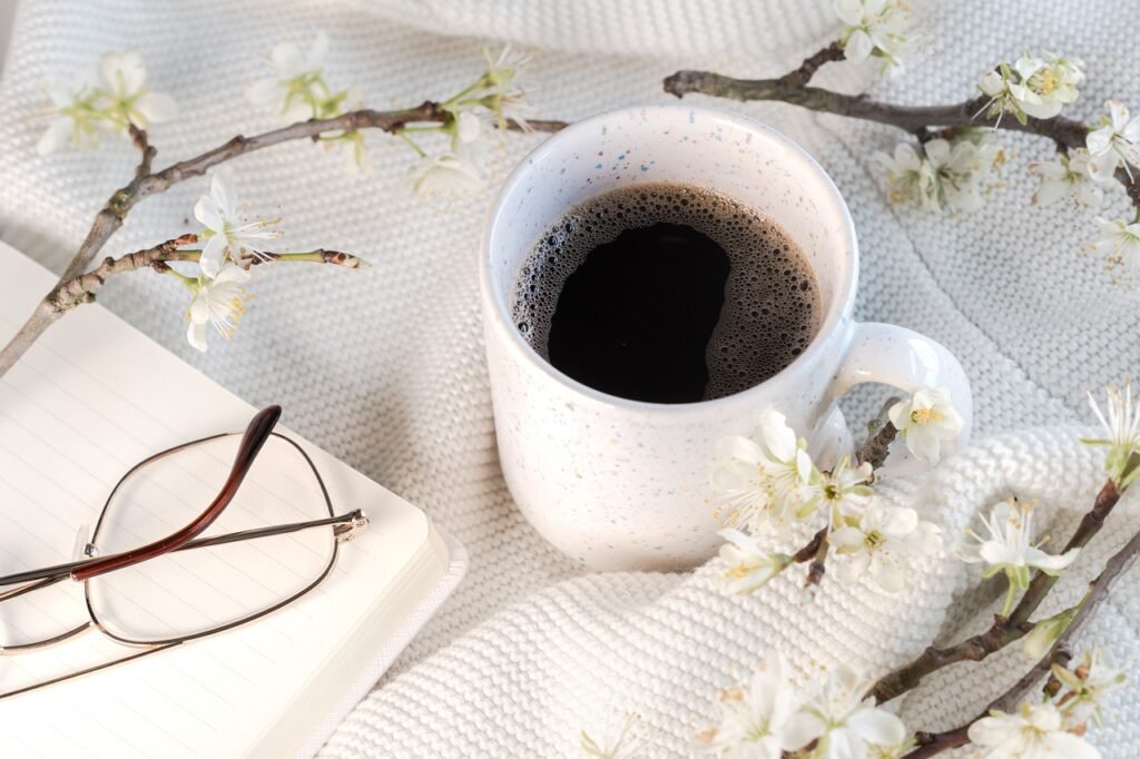 A cozy scene featuring a cup of coffee on a soft blanket, a notebook with reading glasses, and delicate white flowers. The image represents a mother penning her breastfeeding journey, reflecting on moments of self-care and perseverance.