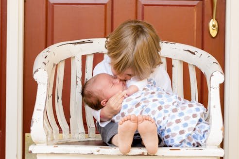 Toddler Carrying and Kissing Baby Sitting on Chair