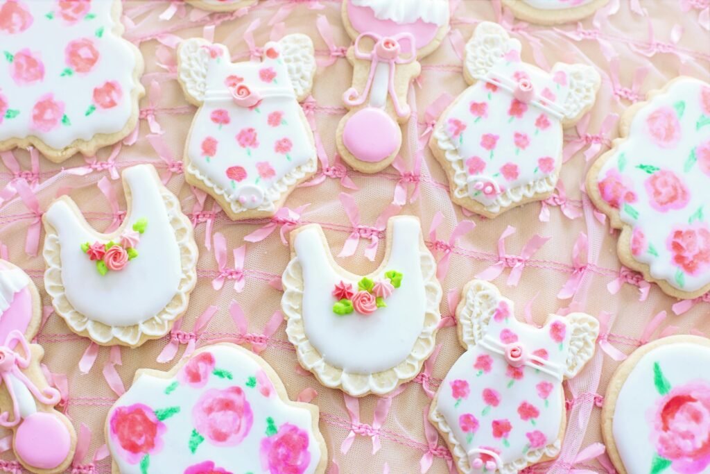 Pink floral baby shower cookies in the shape of bibs and onesies, perfect for a gender reveal baby shower in 2024.