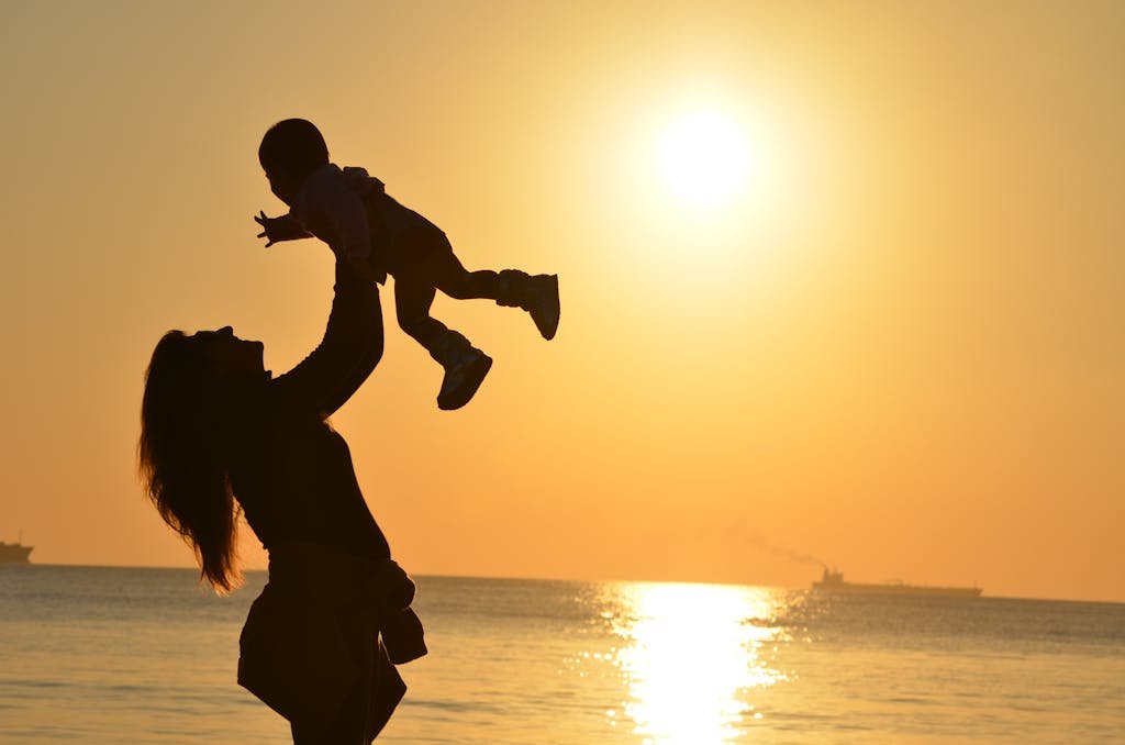 Mother lifting child in joy against a warm sunset, symbolizing strength, love, and the beauty of motherhood.