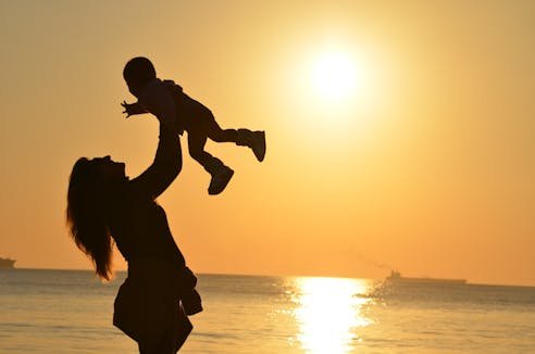 Mother lifting child in joy against a warm sunset, symbolizing strength, love, and the beauty of motherhood.