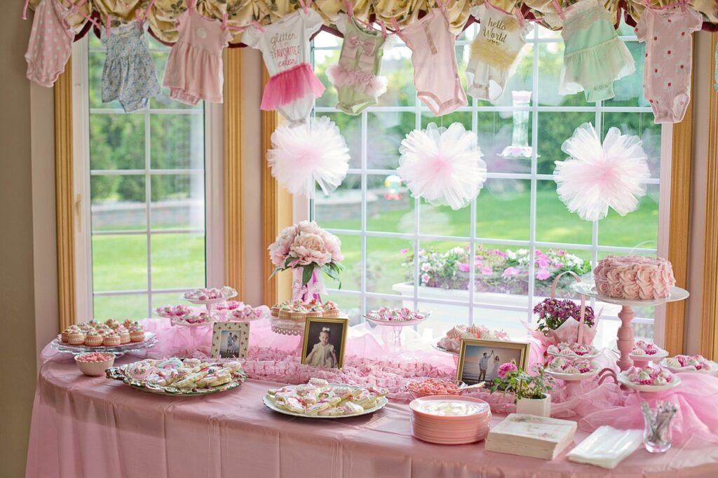 Vintage garden party-themed baby shower table with pink floral decorations, cupcakes, cookies, and baby clothes hanging as décor.